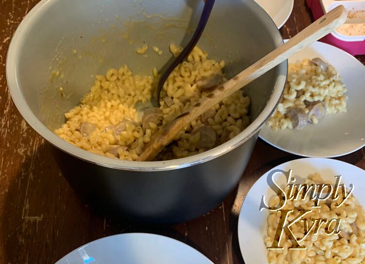 Image shows a pot of pasta with sliced sausage in it. Around the pot are several bowls already dished up.