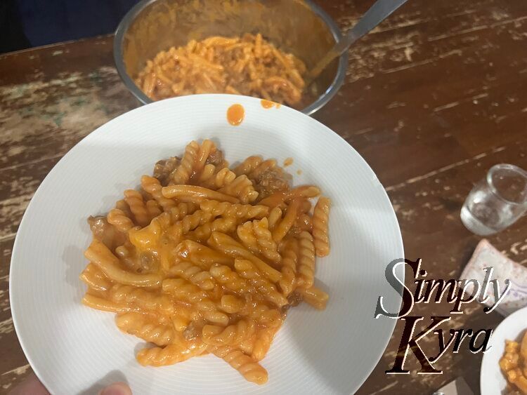 A white bowl filled with cheesy tomato hued pasta.