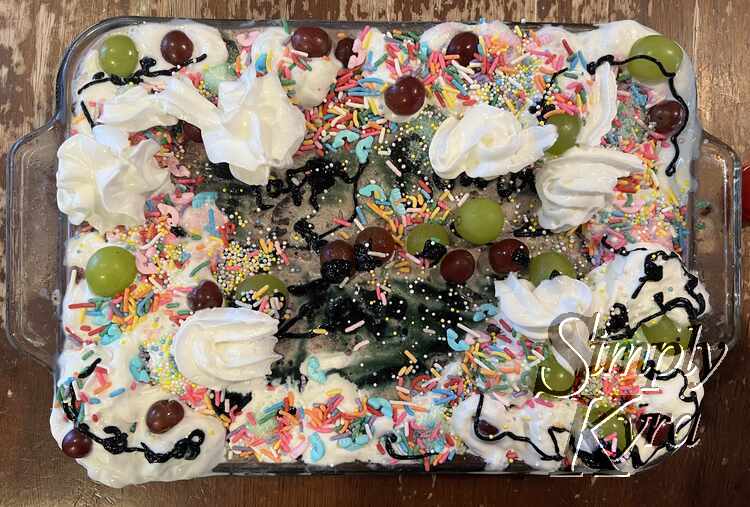 Top down view of the final cake showing the black, whip cream, sprinkle madness, and grape decorations. 