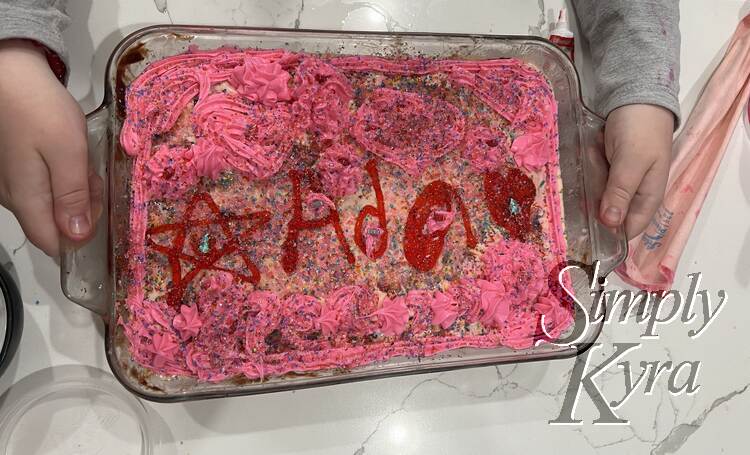 Top down view of the final cake showing the pink piped icing, pink base ice cream, sprinkles, and the red icing written name, star, and heart.