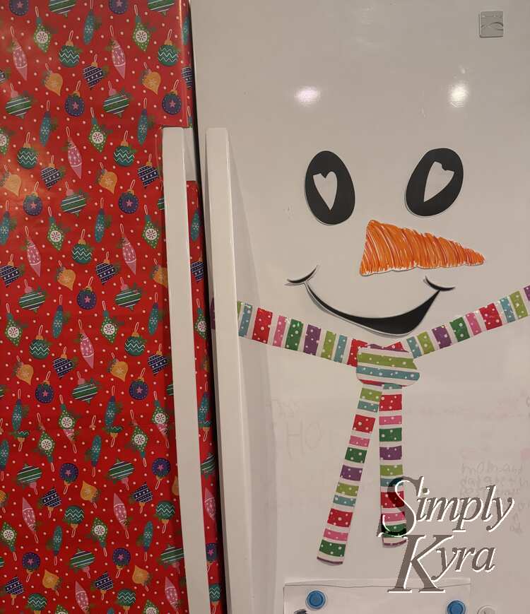 Image shows a closeup of the freezer and fridge with the ornament bedecked red paper on the left and snow person on the right. 