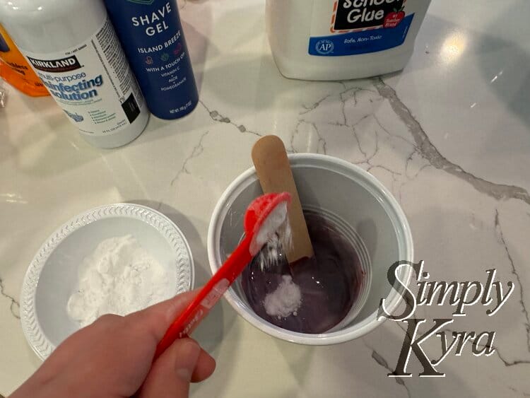 White powder dropping from the red plastic measuring spoon into the cup.