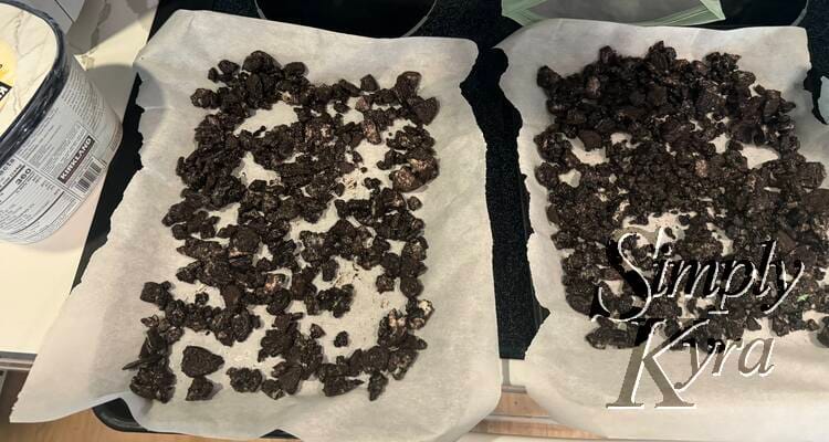 Two small cookie sheets with parchment hold the crushed glistening oreos next to the ice cream container.