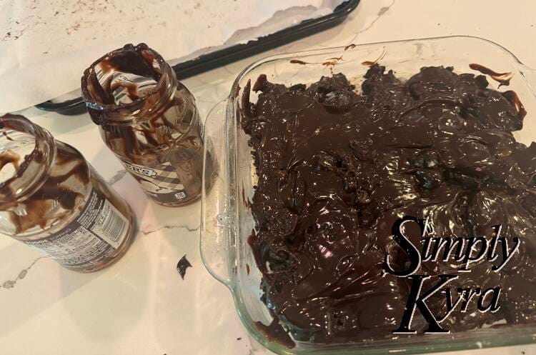 Really fudge coated glass square casserole dish next to two emptly fudge jars.