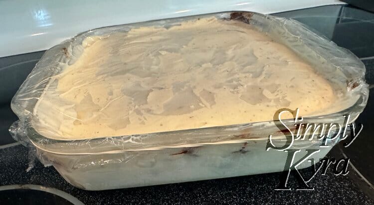 The glass casserole dish topped with plastic wrap and an elastic band holding it on.