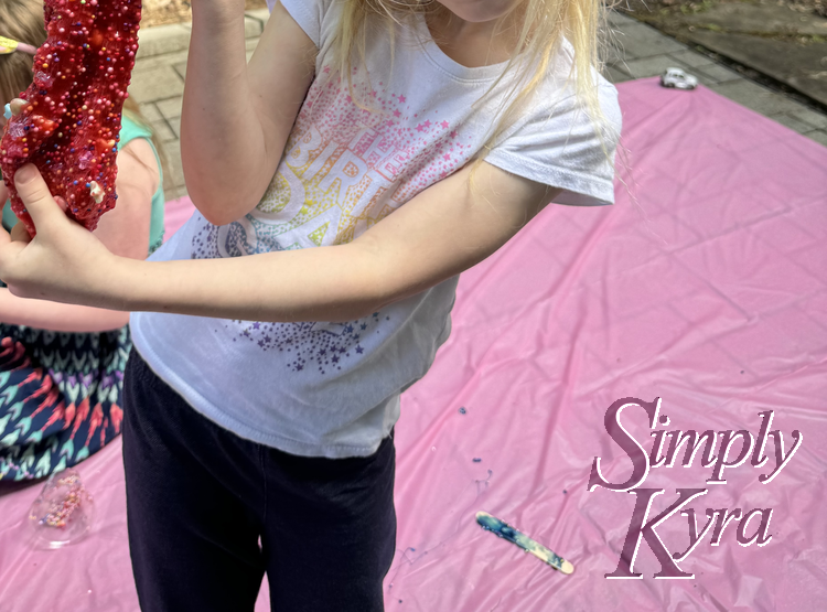 Image shows Zoey stretching her slime with the pink tablecloth and Ada behind.