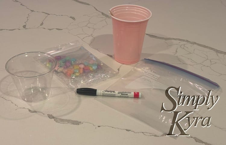 Image shows a pink cup, a small clear one. leftover bagged beads, empty sandwich bag, and black sharpie pen.