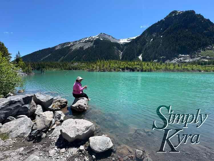 View of me eating on a rock with my feet in the water. Mountains behind.