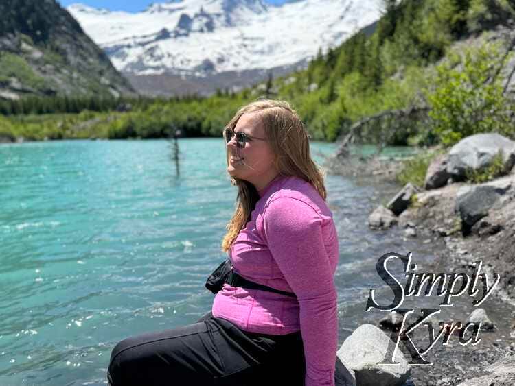 Looking into the distance sitting on a rock by the lake with mountains behind. 