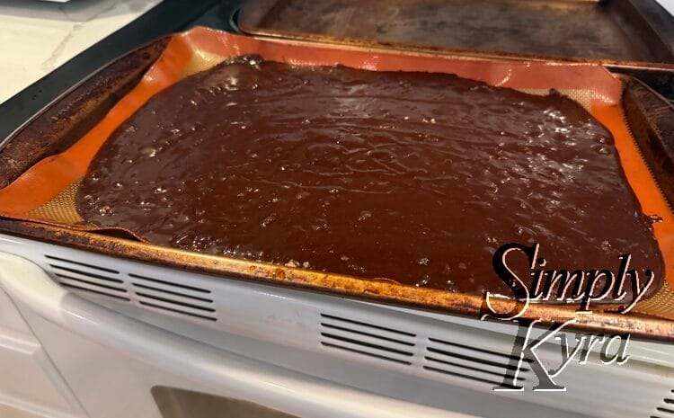 Image shows wet brownie mix spread on orange silpat lined cookie sheet.