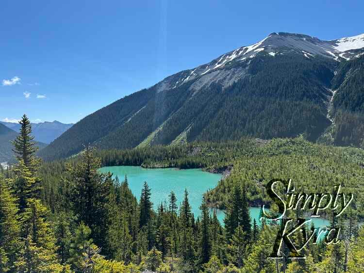 Lake with trees and sunbeam in front and mountains in the background.