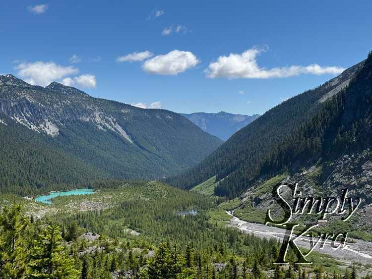 Dab of blue lake against the green trees and hills and blue clouded sky.