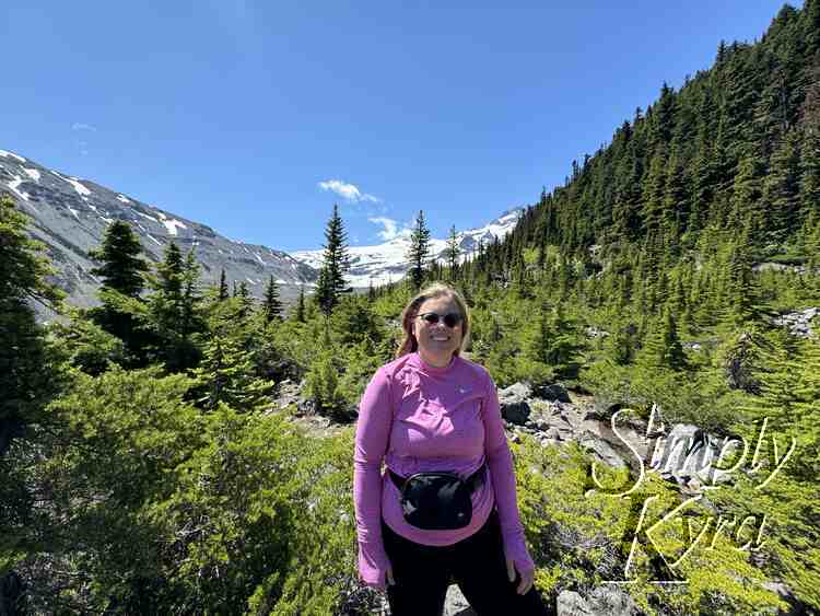 Me looking at the camera with glacier and mountain in background surrounded by trees.