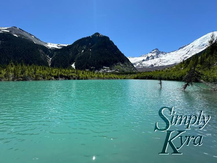 Sparkling mountain lake with trees, mountains, and glacier in background.