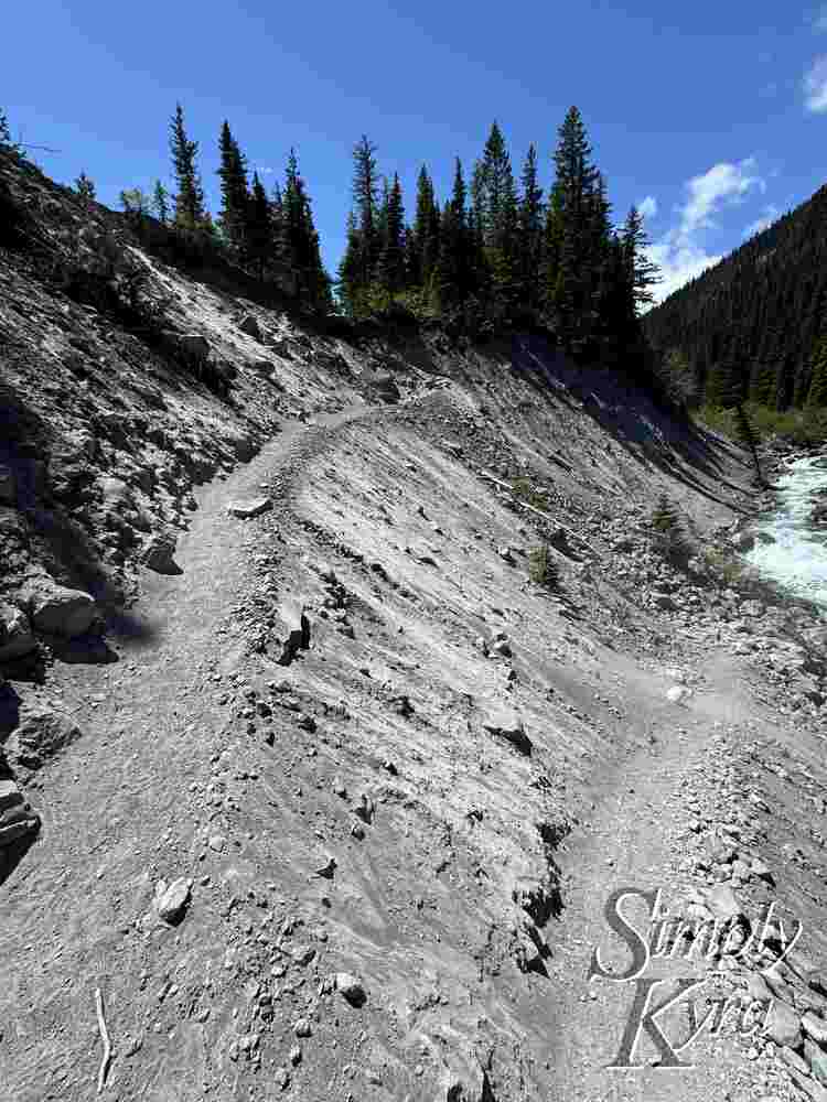 Gravel switchback with dust cloud being blown towards the raging river.