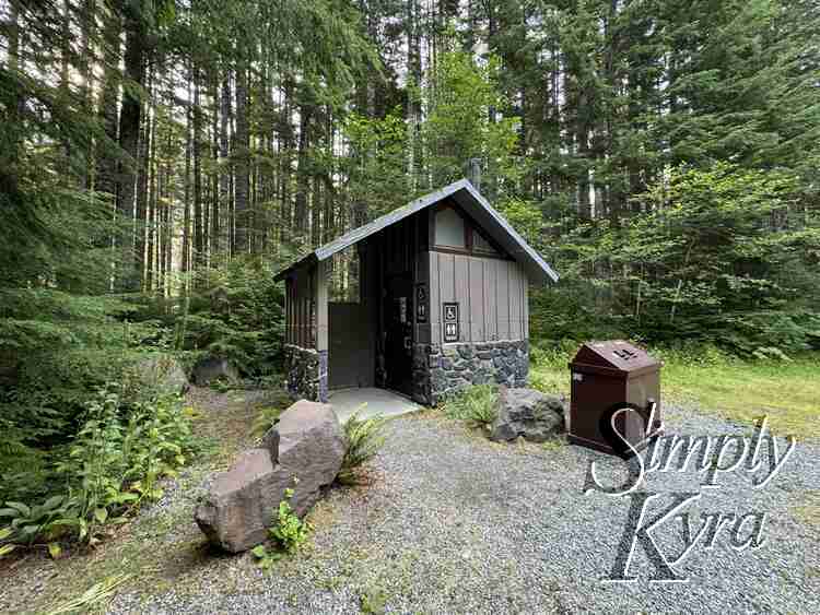 Image of the single stall bathroom with bear-lidded garbage in front surrounded by trees.