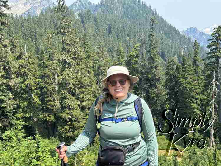 Me smiling at the camera in front of trees and mountains. 