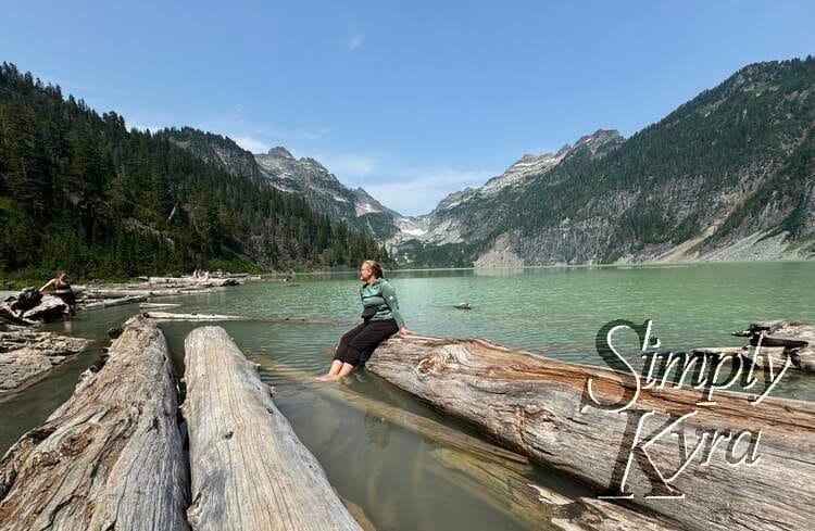 Sitting on a log for a photo framed by the water and mountains.