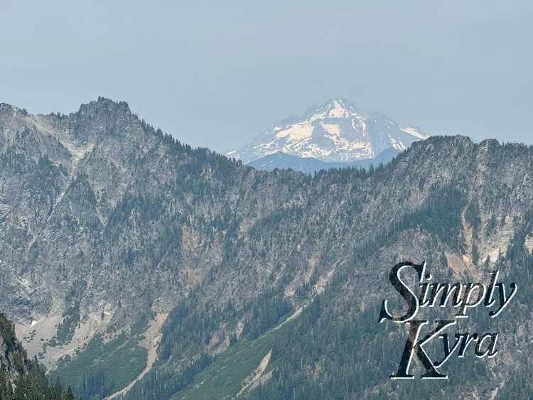 Snow covered mountain peeking above the tree covered ridge.