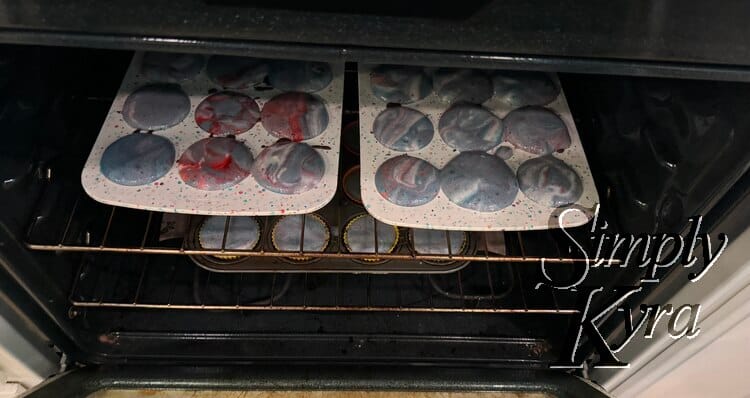 Image looking down at the oven with the silicon liners side by side and metal one below. All have purple, red, blue, and white mixture inside. 