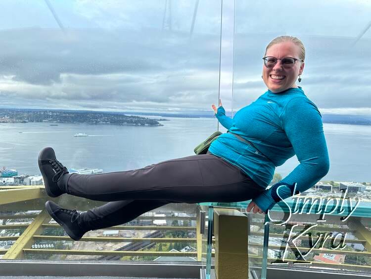 Image shows me sitting on the edge of a glass bench on the Seattle Space Needle with my legs up. 